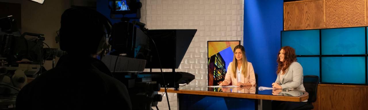 2 student sitting at anchor desk in TV studio